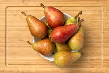 Ripe juicy pears in a bowl on a wooden background, top view