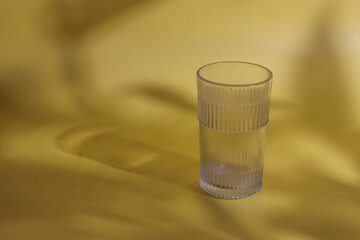 A glass kept on a yellow background with the shadow of a plant