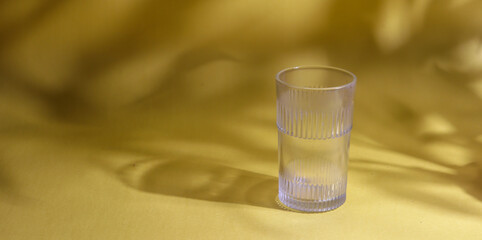A glass kept on a yellow background with the shadow of a plant