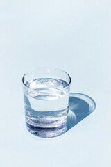 A blue glass of water with sharp strong shadow on blue background with copy space