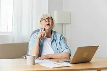 Happy smiling caucasian blonde senior woman sitting at dining table, having video call over at laptop.