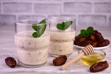 Yogurt and dates and honey in glasses on a white wooden background.
