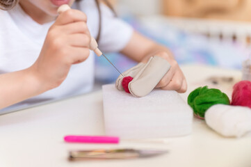 Obraz na płótnie Canvas felt wool craft by handmade with needle. little kid girl artisan nine years old with hand makes a creative toy made of sheep hair. people children hobby and handcraft felting activity