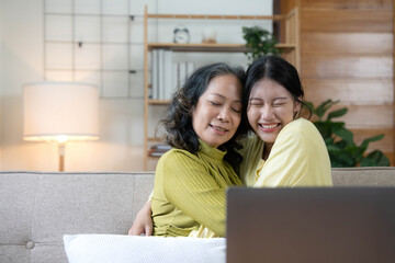 Happy adult granddaughter and senior grandmother having fun enjoying talk sit on sofa in modern living room, smiling old mother hugging young grown daughter bonding chatting relaxing at home together