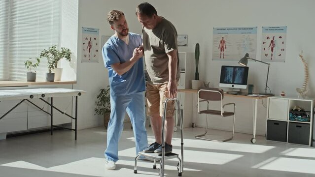 Young doctor in uniform helping patient to stand on the step during his rehabilitation at hospital