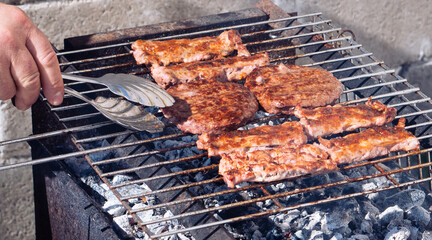 Closeup shot of tasty steaks on barbecue grill, person picking up meat with a steel food tongue