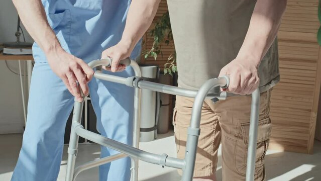 Close-up of doctor helping patient to use walker during his rehabilitation at hospital