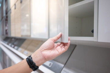 Male hand opening white cabinet door panel in furniture store. Home improvement concept