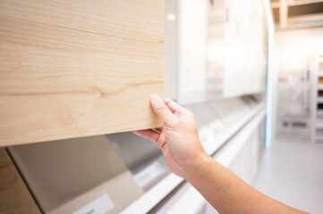 Male hand opening wooden cabinet door panel in furniture store. Home improvement concept