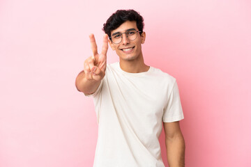 Young Argentinian man isolated on pink background smiling and showing victory sign