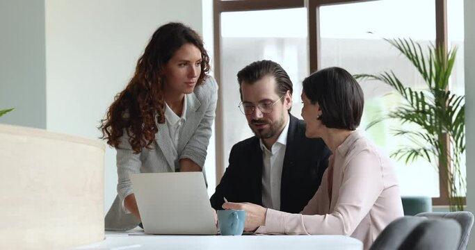 Three businesspeople, millennial and middle-aged colleagues talking staring at laptop screen, discuss app or on-line presentation, work on collaborative project, share ideas take part in group meeting
