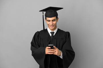 Young Argentinian university graduate isolated on grey background sending a message with the mobile