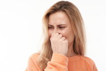 Young blonde woman holding nose to avoid disgusted smell, pinches nose and mouth with fingers and...