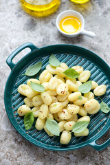 Italian potato gnocchi with fresh basil leaves on a green serving tray, vertical shot on a brown granite background