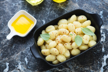 Serving pan with boiled italian potato gnocchi on a black marble background, horizontal shot, elevated view, selective focus