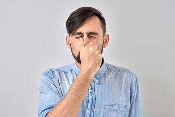 Young man holding nose to avoid disgusted smell, pinches nose and mouth with fingers and holding...