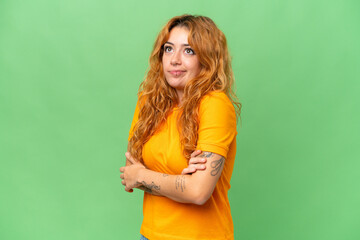 Young caucasian woman isolated on green screen chroma key background making doubts gesture while lifting the shoulders