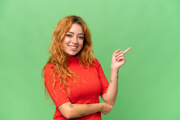 Young caucasian woman isolated on green screen chroma key background happy and pointing up
