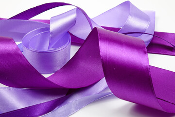 Narrow and wide satin ribbons of different shades of purple color lie randomly on a white background