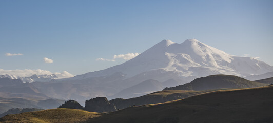 Naklejka na ściany i meble Panorama of Mount Elbrus with two peaks with snow and glaciers, grassy hills in the foreground