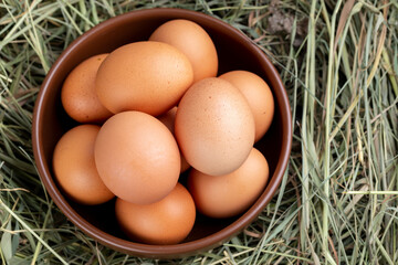 Gray chicken eggs in a clay bowl on a background of hay.