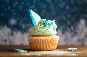 Homemade cupcake of blue color placed on wooden desk. Winter and christmas theme, snowflakes on...