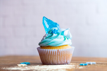 Homemade cupcake of blue color placed on wooden desk. Winter and christmas theme, snowflakes on cream with blue ice. Fresh and home baked sweet.