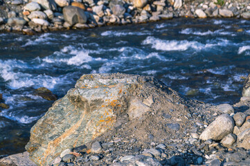 Fototapeta premium The stone lies near a mountain river. A large rock of solid rock in the mountains. Nature in the mountains.