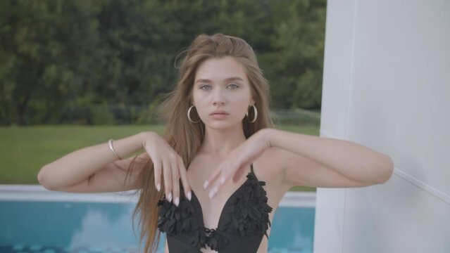 Model girl with long hair in a black swimsuit poses and raises her hands against the sky 