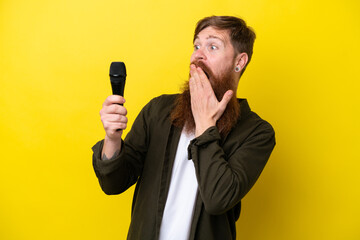 Naklejka premium Redhead man with beard picking up a microphone isolated on yellow background with surprise and shocked facial expression