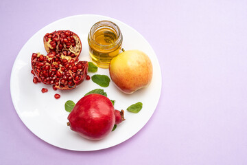 Jewish New Year Rosh Hashanah Traditional purple background with apples, pomegranate and honey on a plate