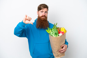 Redhead man with beard holding a grocery shopping bag isolated on white background showing thumb down with negative expression