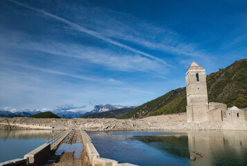 Fototapeta premium The reservoir with the tower of the church of the Assumption emerged due to drought and lack of rainfall. Climate change. Autumn 2022. Huesca, Spain.
