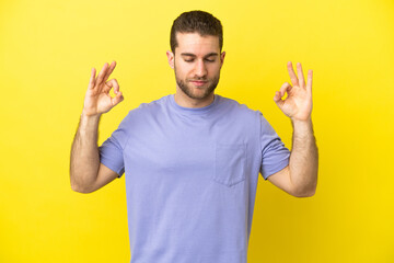 Handsome blonde man over isolated yellow background in zen pose
