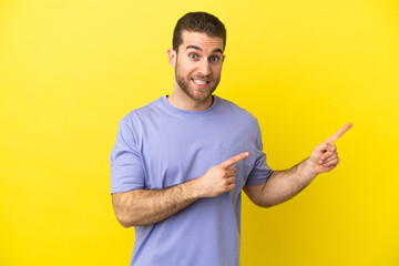 Handsome blonde man over isolated yellow background frightened and pointing to the side