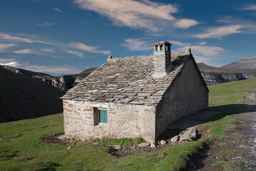 The Plana Canal Refuge is a livestock shelter with the mountains in the background. The three...