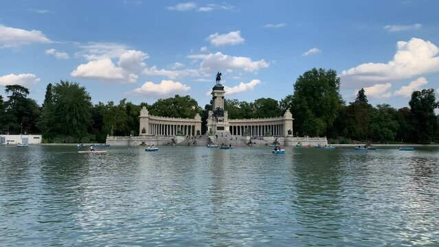 Tiny boats are moving in a big pond, lake at the Buen Retiro Park (Parque del Buen Retiro). Alfonso XII monument in the background. Motion of water. Popular recreation place. Madrid, Spain