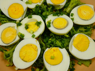Halves of boiled chicken eggs sprinkled with green onions lying on green leaves of fresh lettuce 