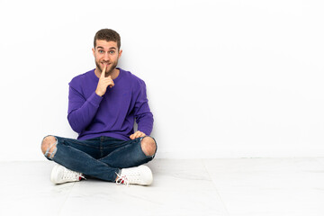 Young man sitting on the floor showing a sign of silence gesture putting finger in mouth