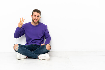 Young man sitting on the floor happy and counting three with fingers