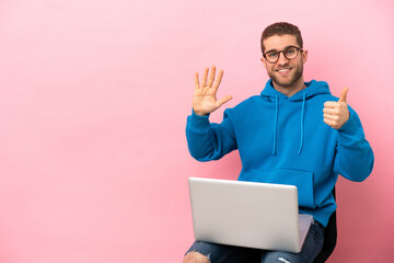 Young man sitting on a chair with laptop counting six with fingers