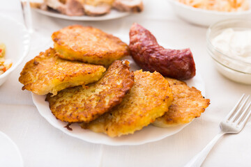 Fried grated potato pancakes with fried sausage on white plate