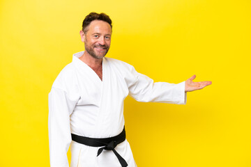 Middle age caucasian man doing karate isolated on yellow background extending hands to the side for...