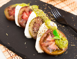 caprese salad with mozzarella, black tomatoes and pesto on black stone plate