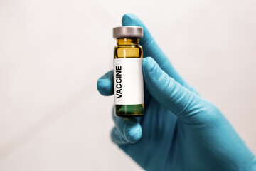 Hand of a doctor with a blue glove showing the vaccine vial with a label, Vaccine bottle. Vaccine for the disease, drug concept.
