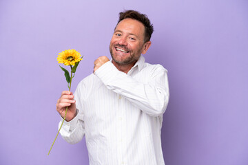 Middle age caucasian man holding sun flower isolated on purple background celebrating a victory