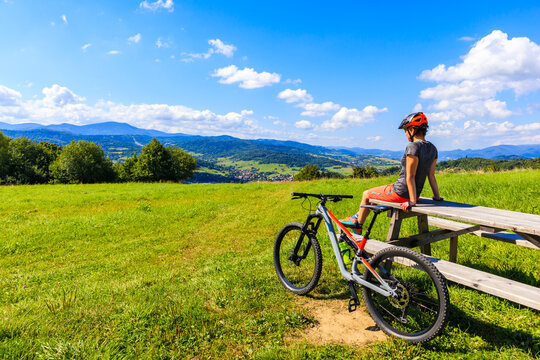 Woman mountain biker sitting on wooden table on green meadow in summer, Beskidy Mountains near Zywiec, Poland