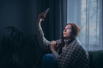 A young woman is trying to catch a connection during a power outage. The female sits on a couch in...
