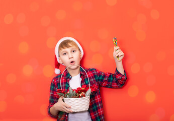 Cute caucasian kid teenager boy in red Santa's hat holds festively decorated basket and candy cane on red background. Copy space for design or text. Banner. Christmas New Year mockup template.