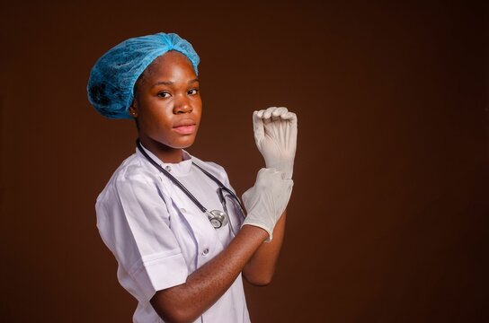 Smiling Nigerian female medic putting gloves on her hands on a brown background